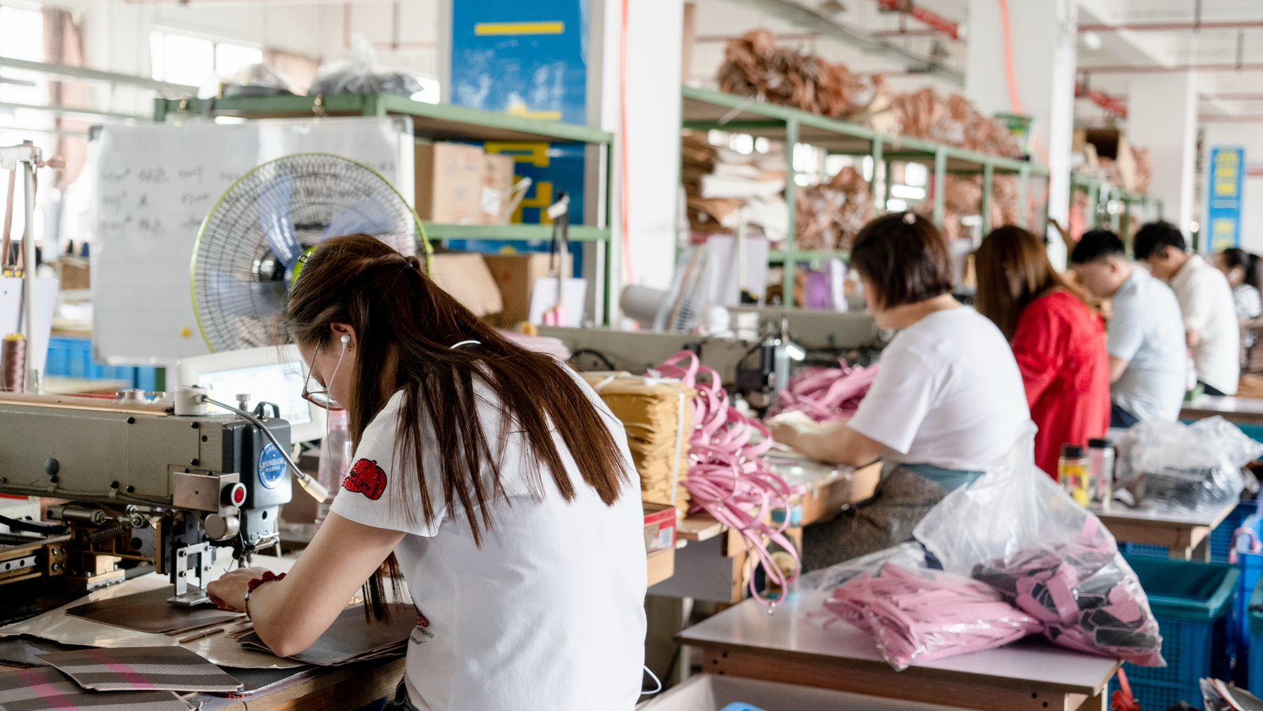 A worker sewing pink bag material at a machine