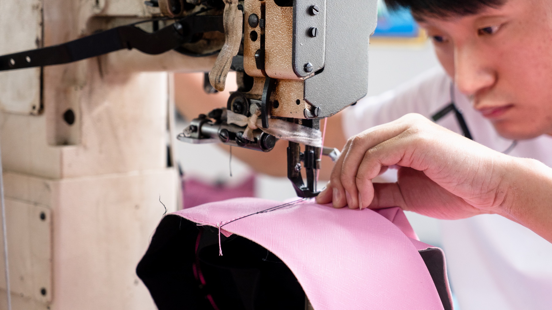 Close view of a worker sewing pink bag material